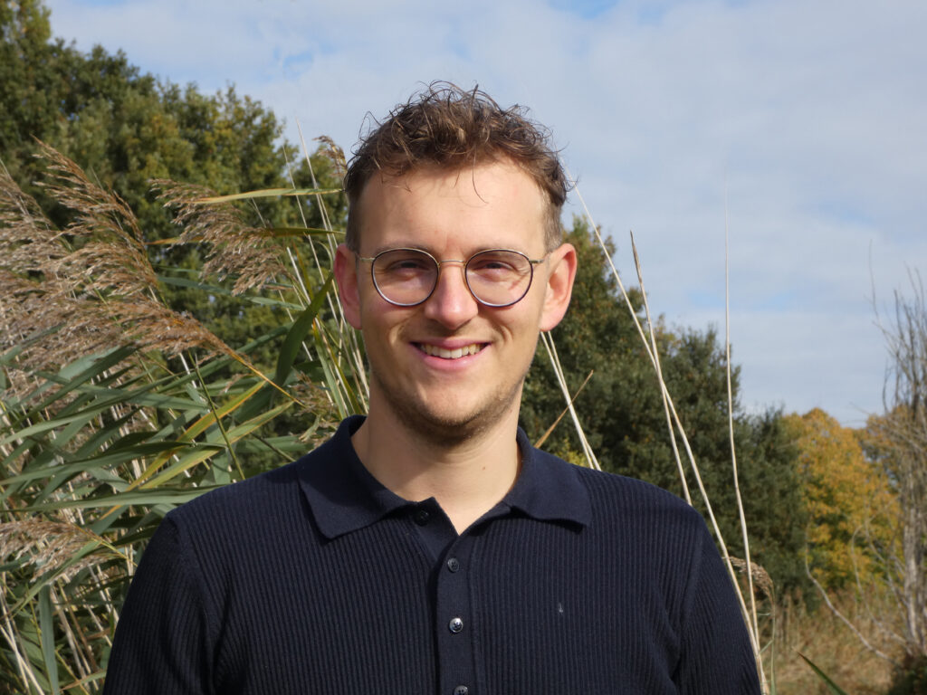 Lijsttrekker Kevin Bax staat buiten in de natuur en kijkt lachend naar de camera.