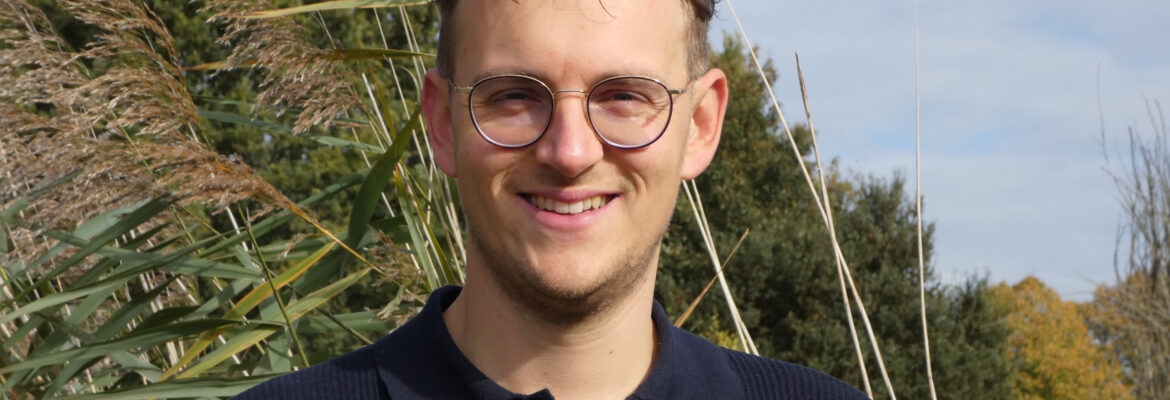 Lijsttrekker Kevin Bax staat buiten in de natuur en kijkt lachend naar de camera.