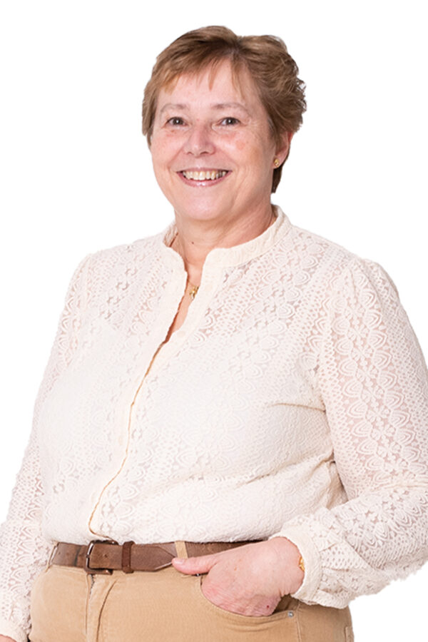 May van Lierop kijkt je lachend aan. Ze heeft een hand in haar broekzak en draagt een lichte blouse met lichtbruine broek.