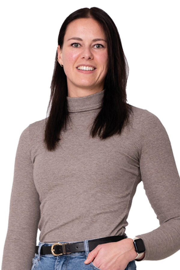 Nikki Turkenburg kijkt je lachend aan. Ze heeft een hand in haar broekzak en draagt een lichtbruin truitje en een spijkerbroek.