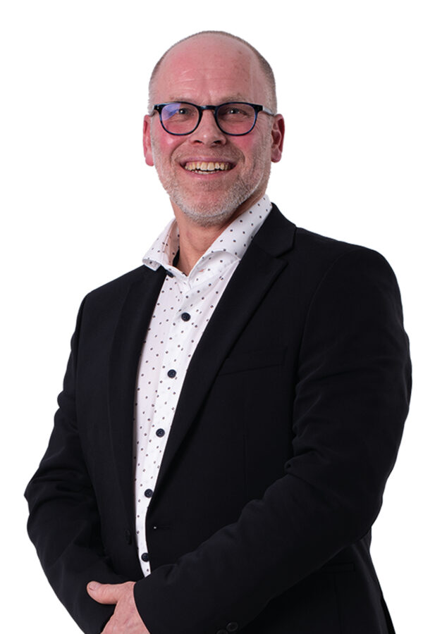 Jan-Willem van Gog kijkt je lachend aan. Hij draagt een wit overhemd en een donkerkleurig colbert