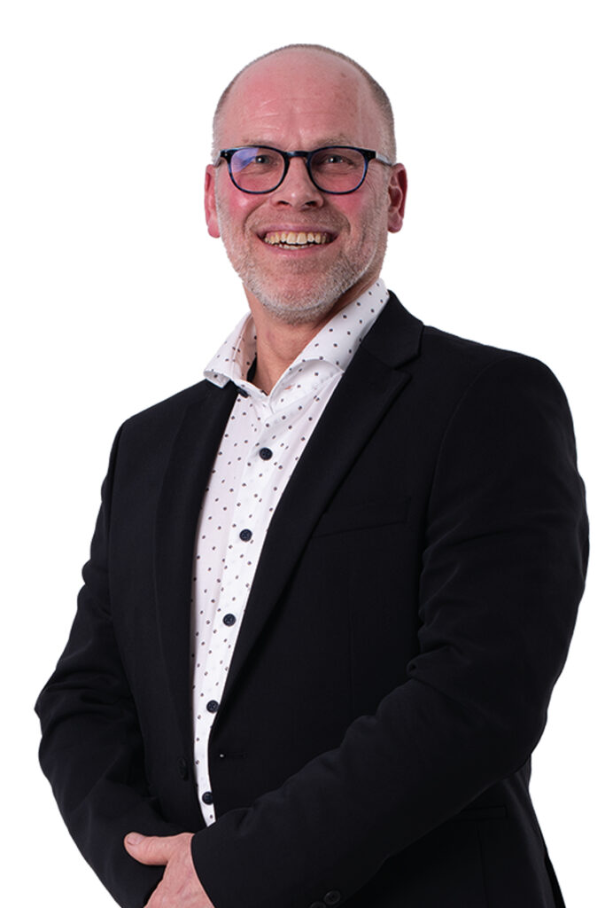 Jan-Willem van Gog kijkt je lachend aan. Hij draagt een wit overhemd en een donkerkleurig colbert