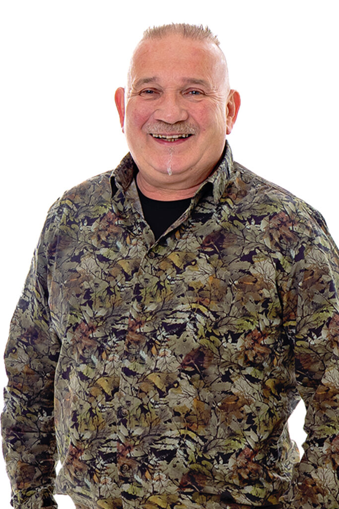 Jan Smeets kijkt je breedlachend aan. Hij draagt een groene blouse met motief.